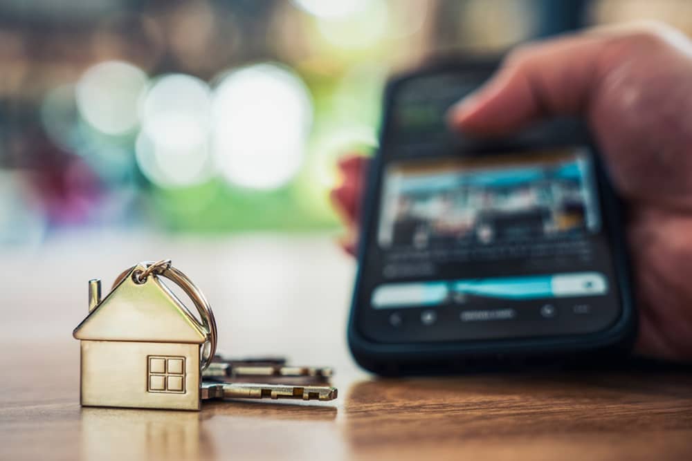 Person browsing a real estate listing on a smartphone next to a house-shaped key chain